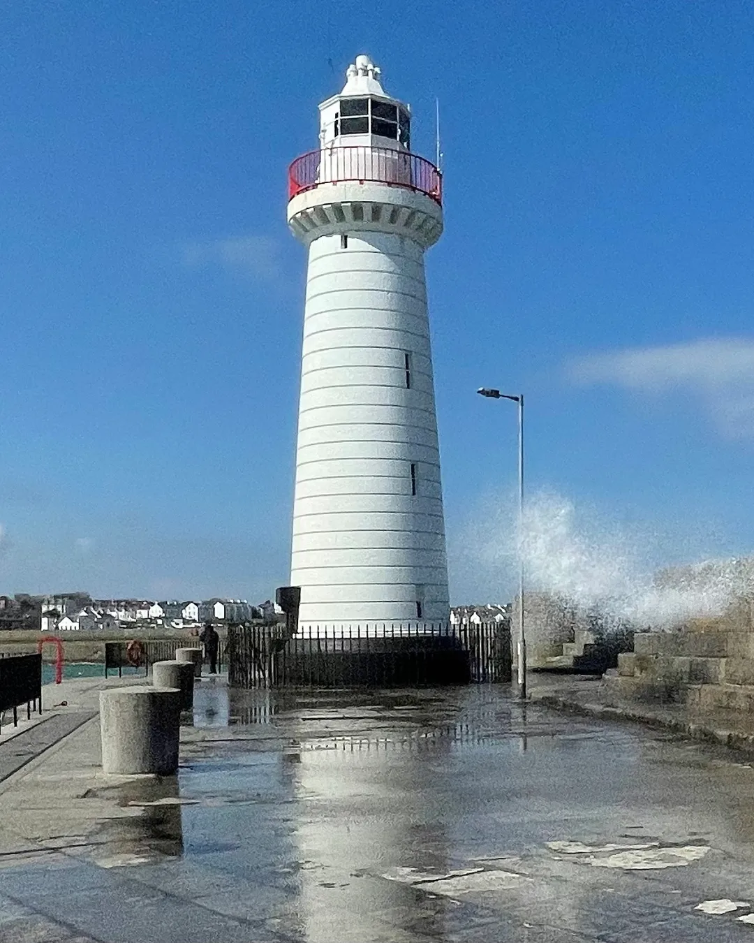The distinctive white Donaghadee Lighthouse with its black cap, standing at the end of the long stone pier under a blue sky, Northern Ireland.